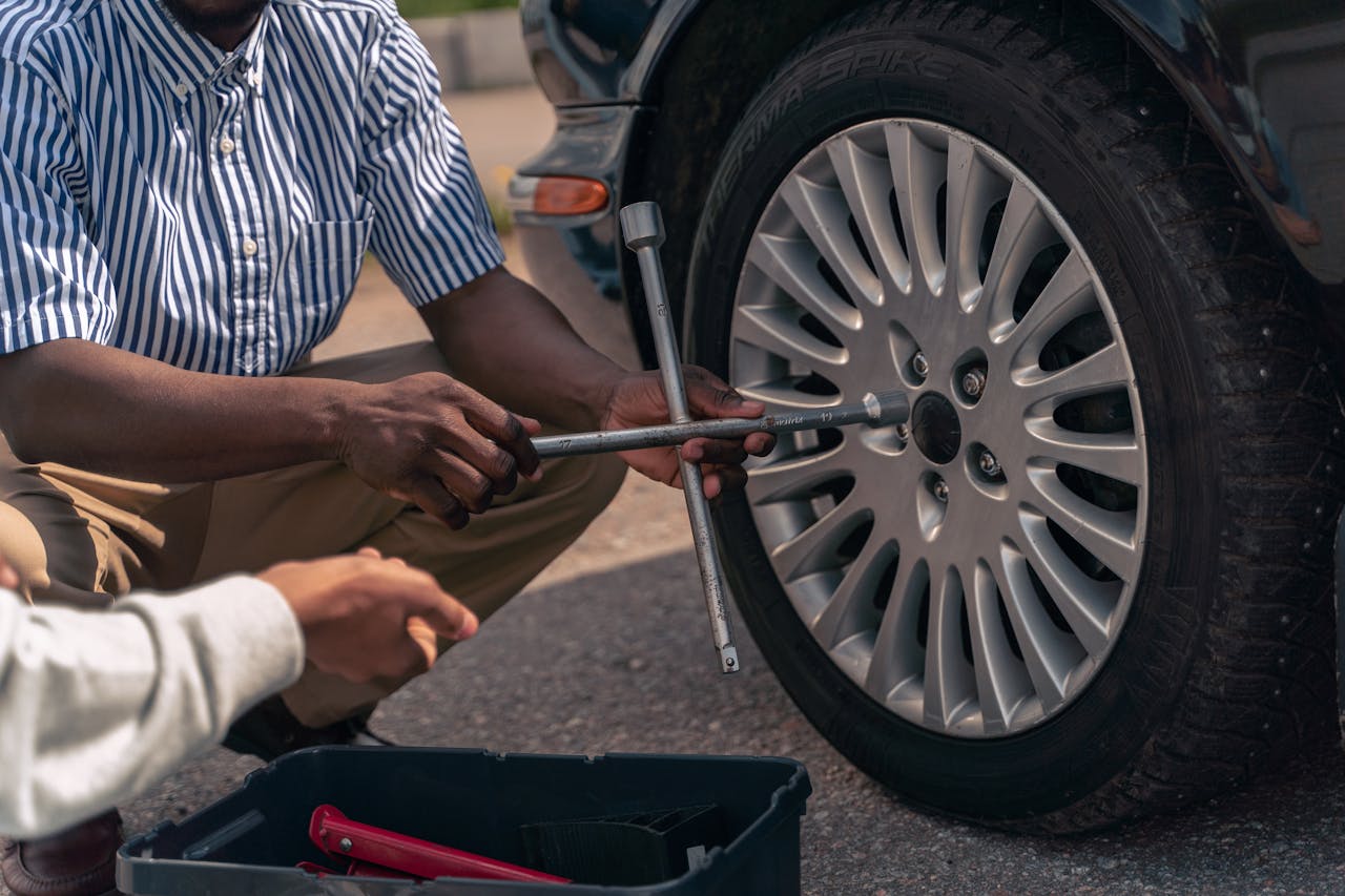 our-stories An adult demonstrating how to change a tire to a teenager, focusing on teamwork and learning.